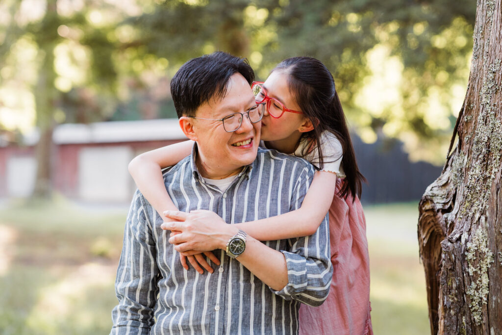 Daughter kissing dad’s cheek during a playful sunset family shoot in Riverhead Forest, West Auckland.