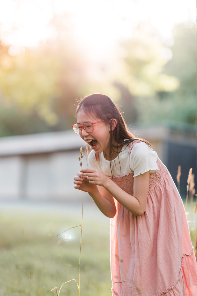 Girl blowing a dandelion on her own in Riverhead Forest with soft sunset light – whimsical family photography Auckland.