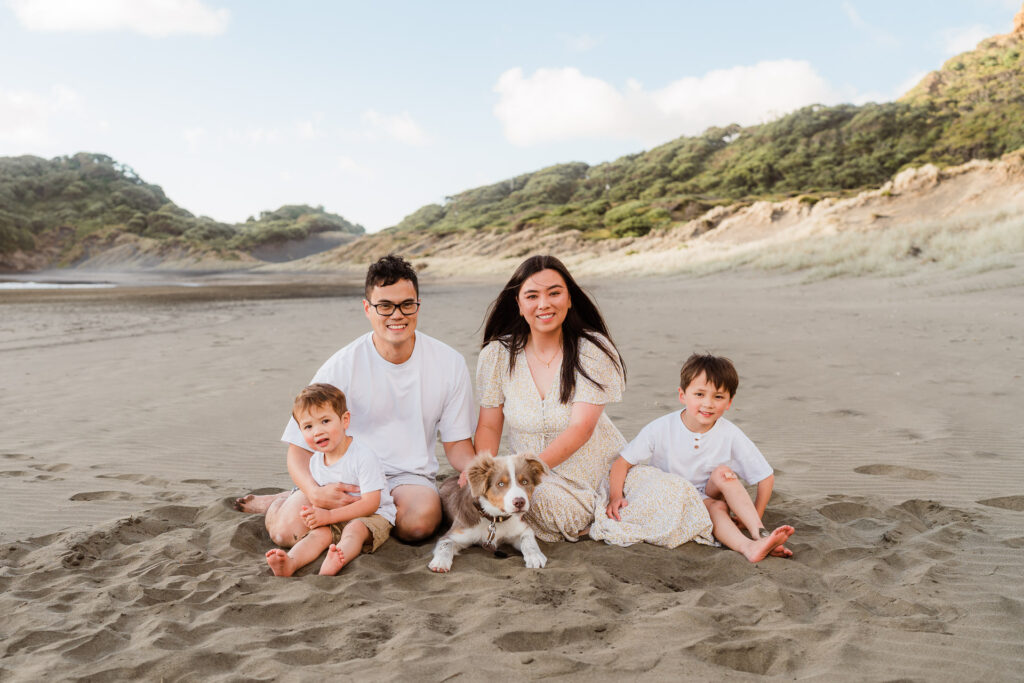 Family of four sitting together on the sand at Bethells Beach – candid family portrait in West Auckland.