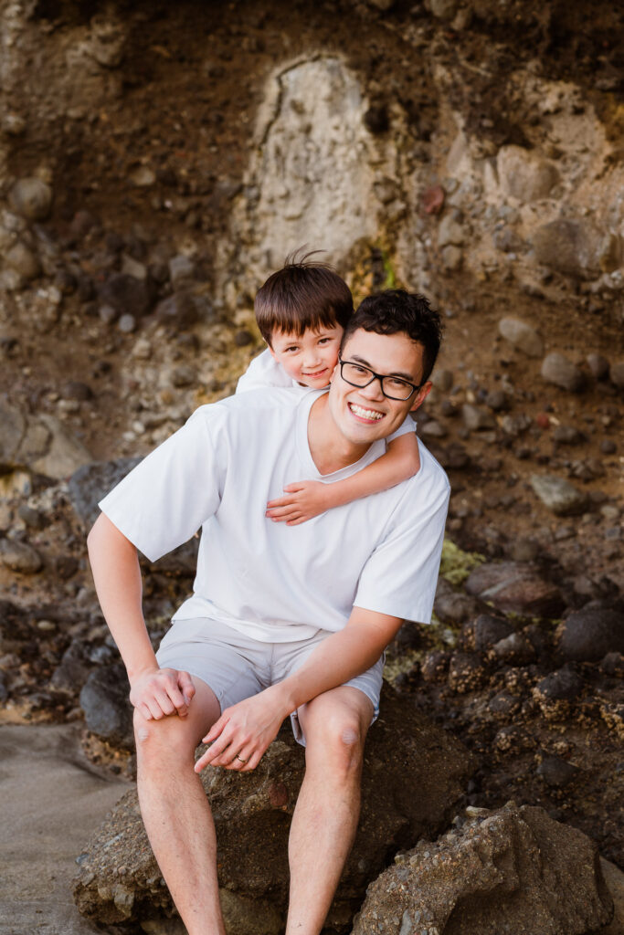 Dad and son sharing an over-the-shoulder cuddle during a sunset family shoot at Bethells Beach – warm family moments in West Auckland.
