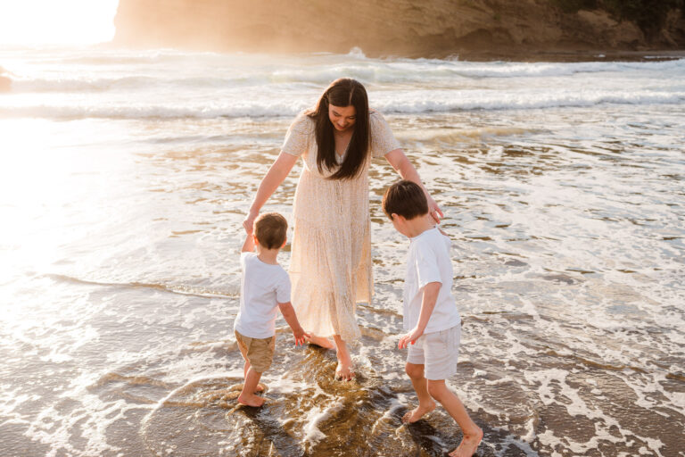 Parents watching children play at sunset on Bethells Beach – natural family moments captured in West Auckland.