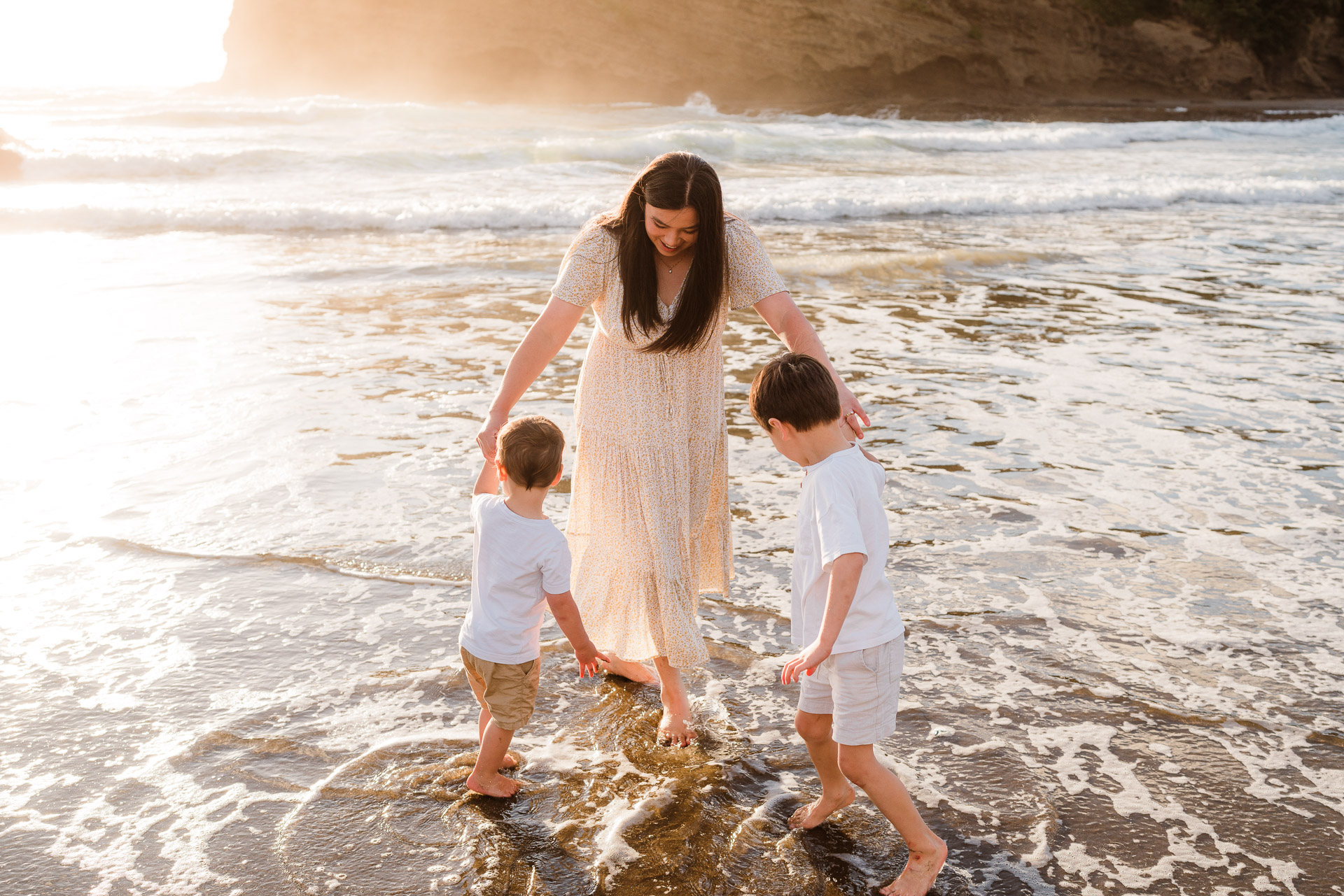 Parents watching children play at sunset on Bethells Beach – natural family moments captured in West Auckland.