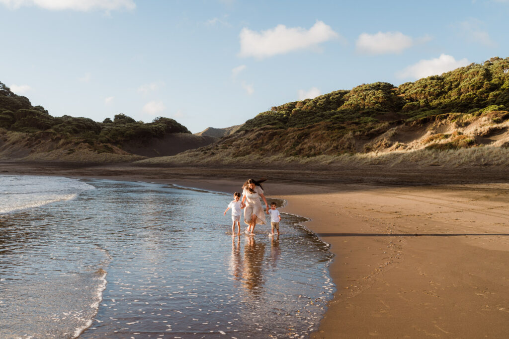 Two boys playing and running on the sand at Bethells Beach – fun, playful family photography in Auckland.