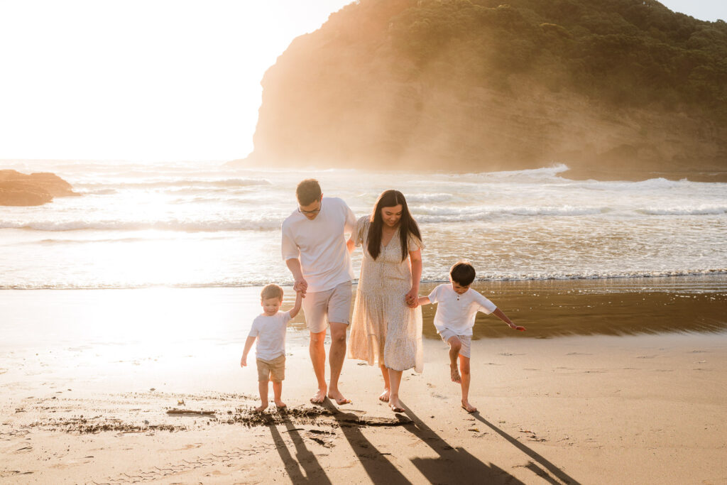 Family of four walking along Bethells Beach at sunset – relaxed West Auckland family photography.