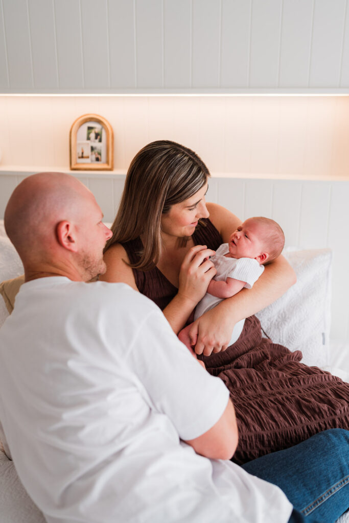Mum, dad, and newborn cuddling together on the bed during a lifestyle newborn session in Auckland.