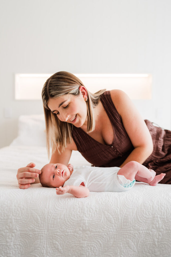 Mum holding newborn baby on the bed during a lifestyle session at their Auckland home – warm and intimate family photos.