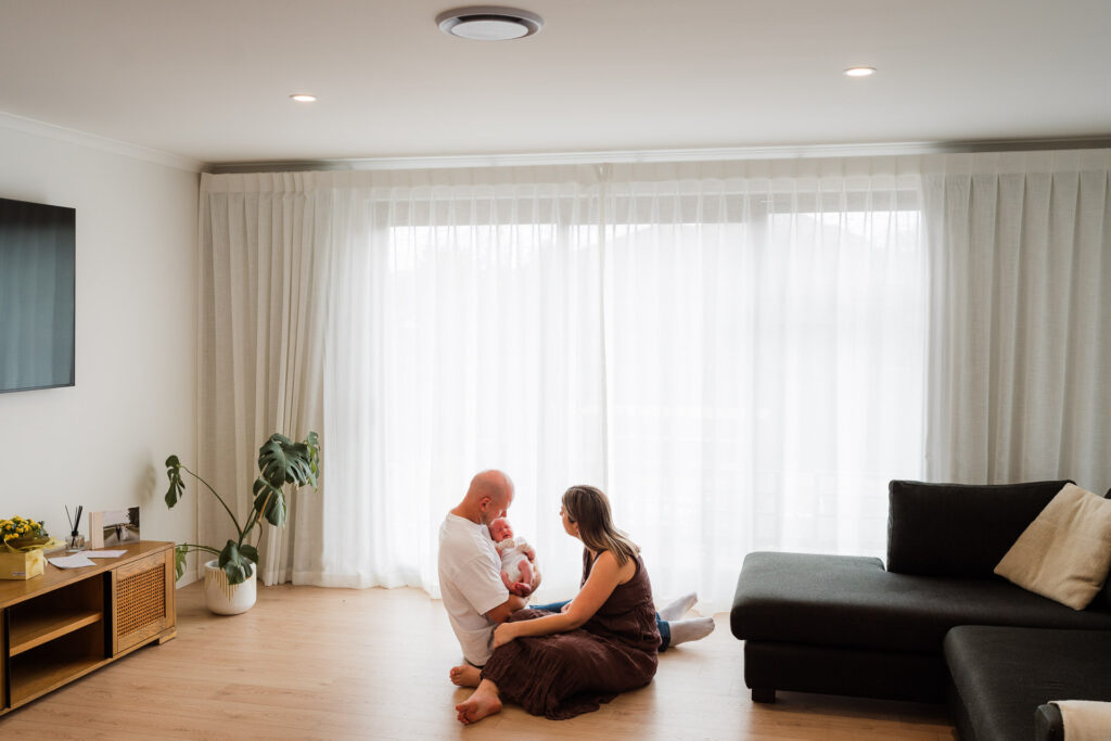 Wide shot of the family together in the lounge during a lifestyle newborn session at home in Auckland – natural and candid photography.