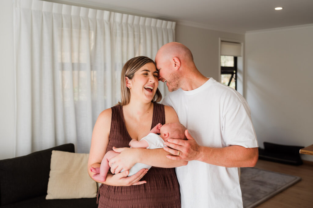 Dad kissing mum while all three share a tender moment during a lifestyle newborn shoot at home in Auckland.