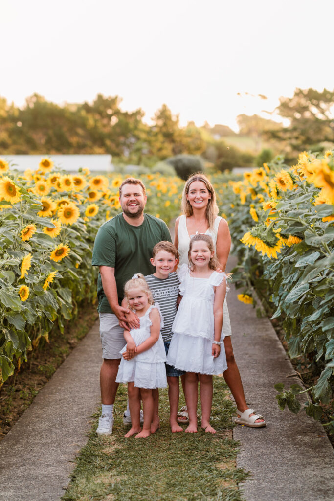 Family standing together in a sunflower field during a mini session at Franklin Farms in Waimauku, photographed by Wonderferris.
