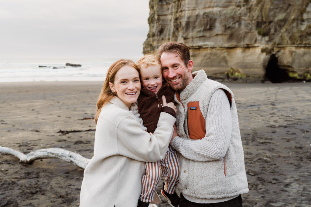 Natural family photo with parents and children sitting on the sand at Muriwai Beach.