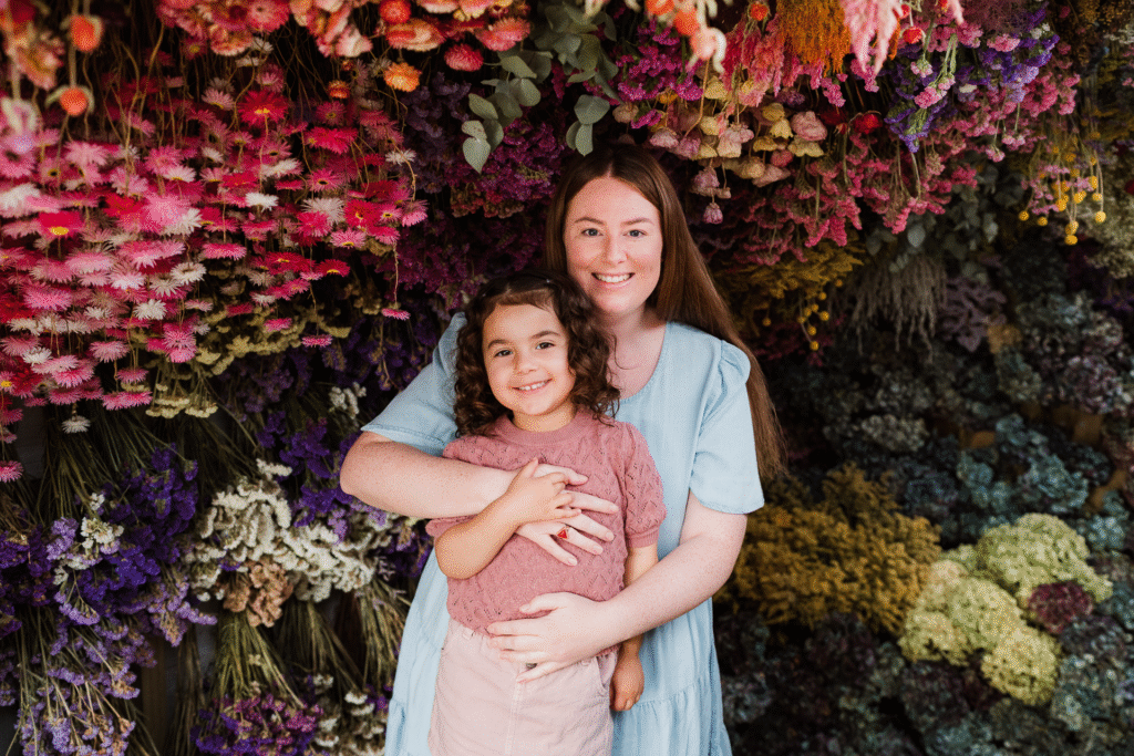 Playful shot of toddler interacting with dried florals while cuddled up with mum in West Auckland.
