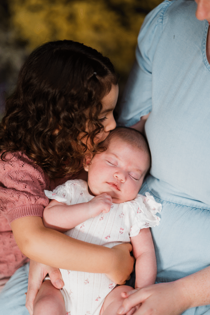 Sweet moment of two sisters kissing in a dried flower-filled workshed at a Taupaki mini shoot.