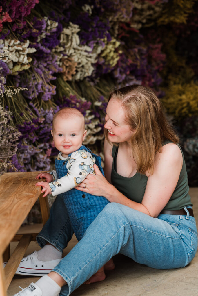 Candid moment of mother and baby cuddling in a florist shed filled with dried florals, photographed by Wonderferris.