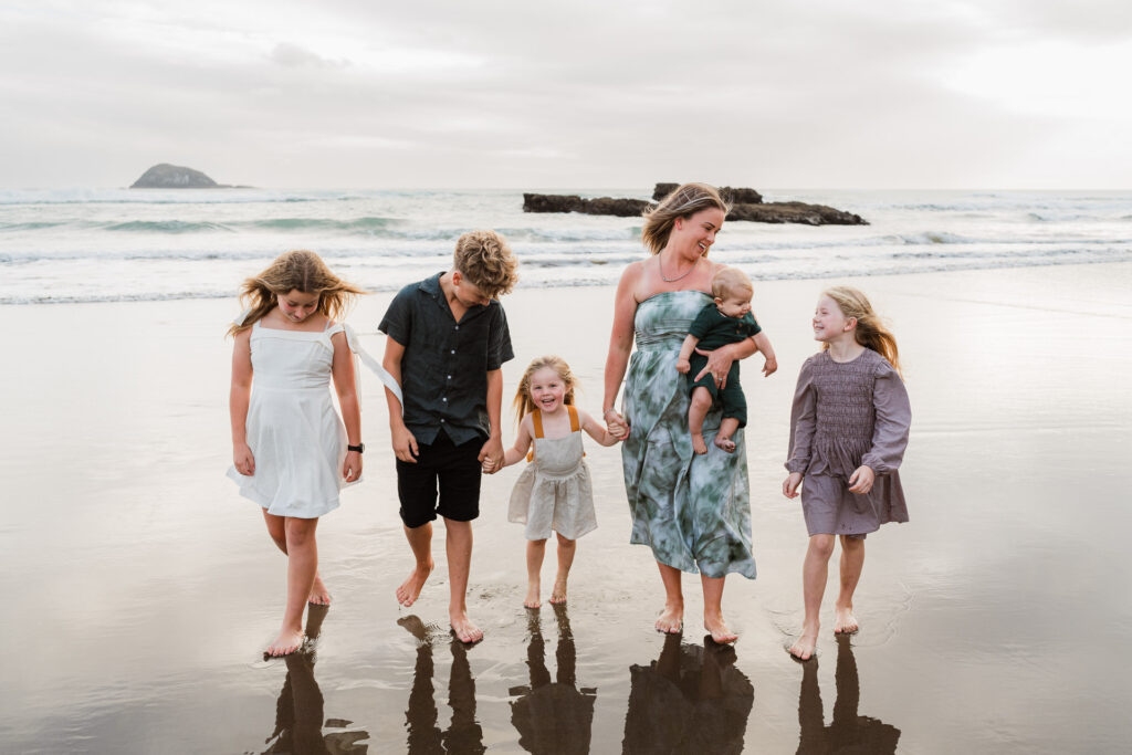 Natural walking shot of mum and her children at an Auckland beach mini shoot, showing movement and connection.