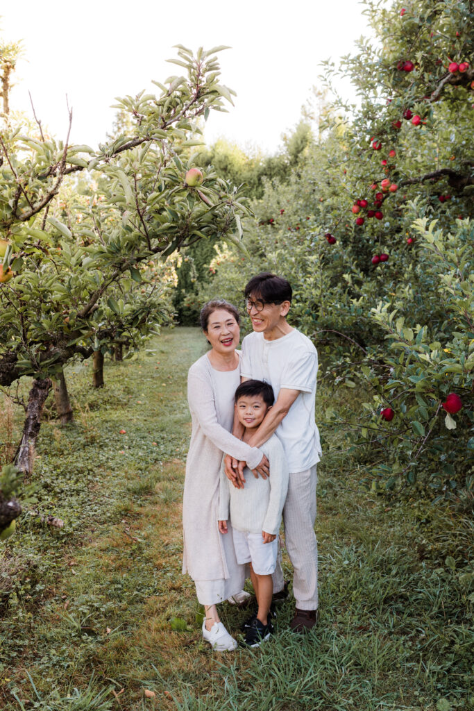 Natural family photo of grandparents and grandchild smiling together at a NorthWest Auckland orchard.
