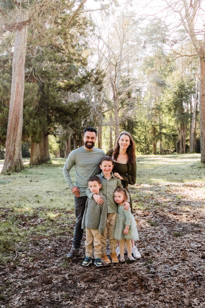 Family of four standing together in Riverhead Forest, smiling at the camera — captured by Auckland family photographer