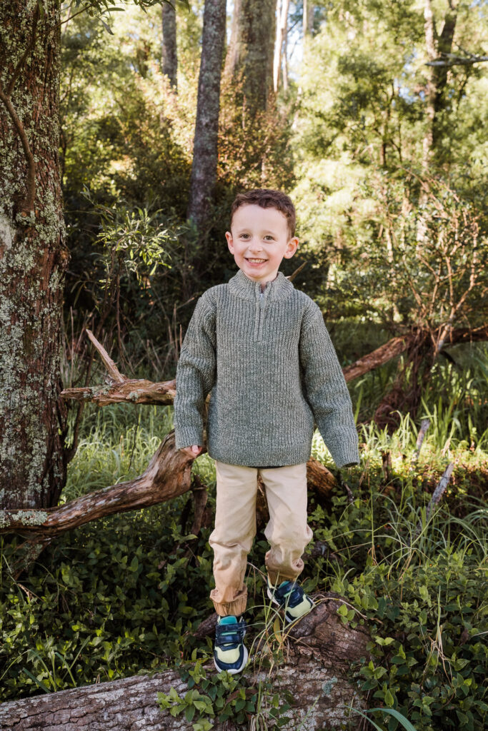 Close-up of boy smiling, trees softly blurred in the background — Kumeu family photographer