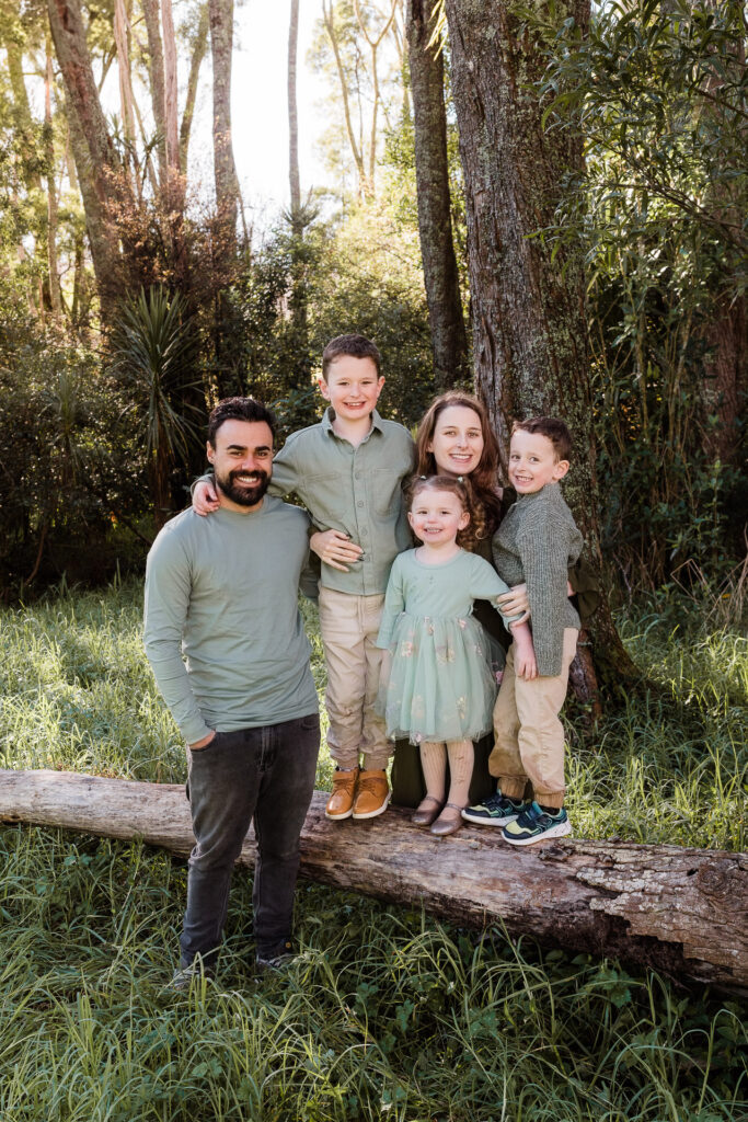Family of five walking through Riverhead Forest, all smiling at the camera — Auckland family photographer