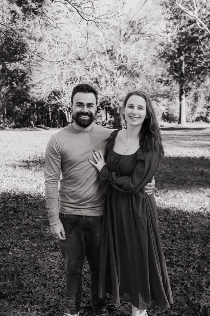 Couple standing close together in Riverhead Forest, smiling at each other — captured by West Auckland family photographer