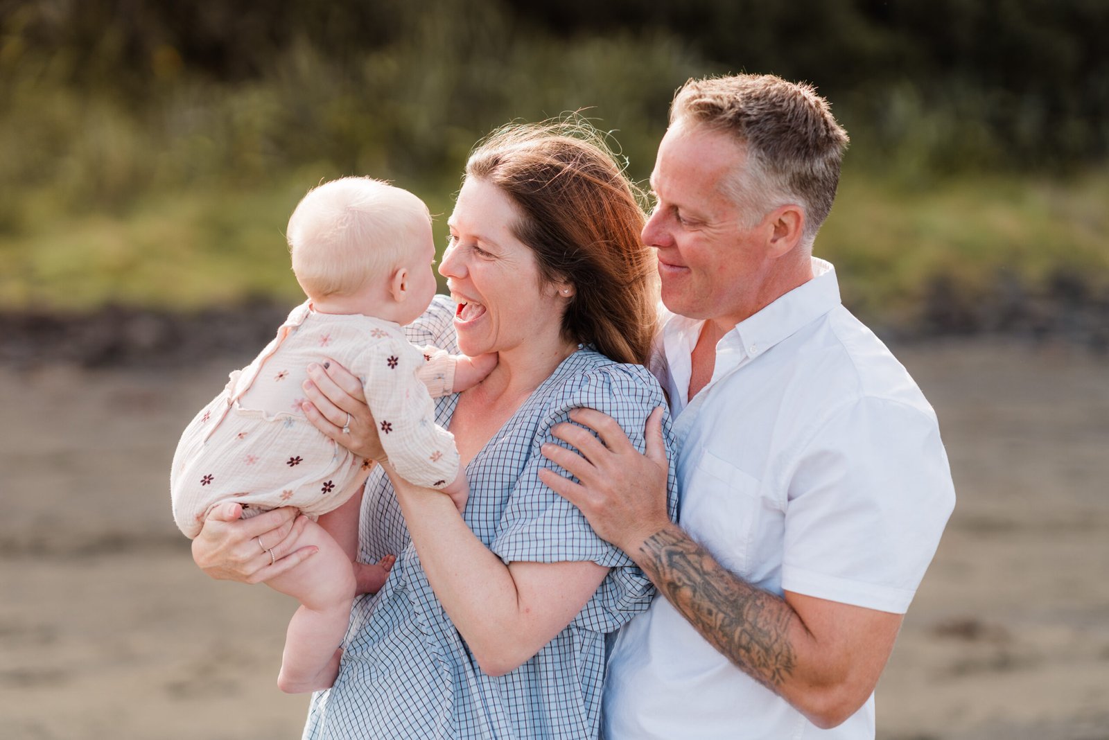 Smiling couple holding their baby outdoors at the beach, embracing warmly.