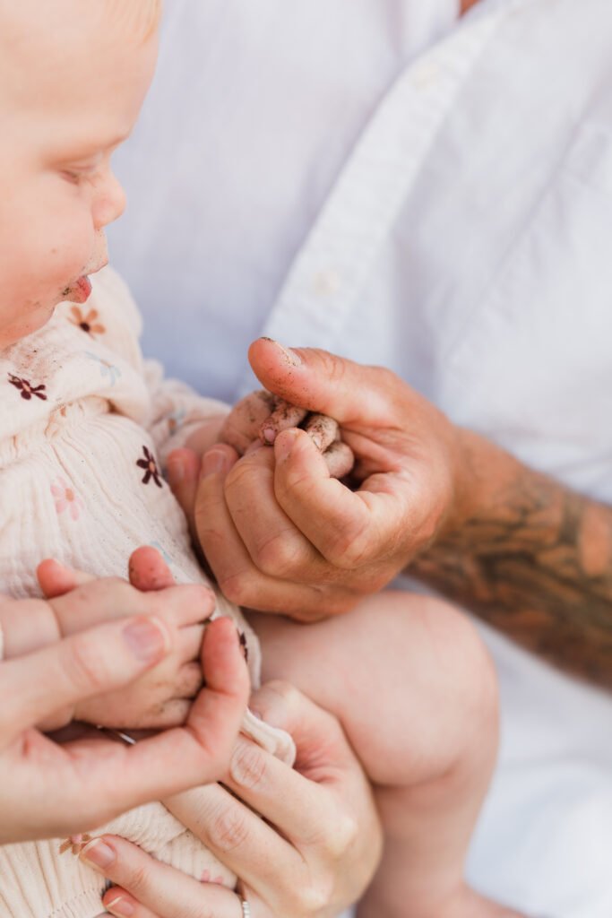 Close-up of a baby being cradled by an adult, with dirt on the baby's and caregiver's hands and a gentle touch.
