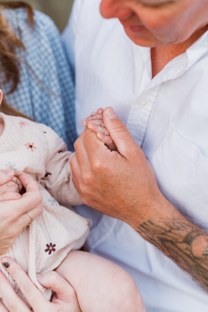 Adult hand gently holds a baby's tiny hand, showing a loving, protective moment.