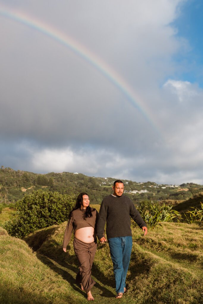 Pregnant couple walking outdoors under rainbow in countryside