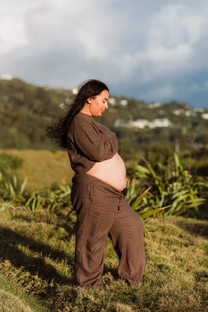 Pregnant woman standing outdoors in brown clothing, smiling.