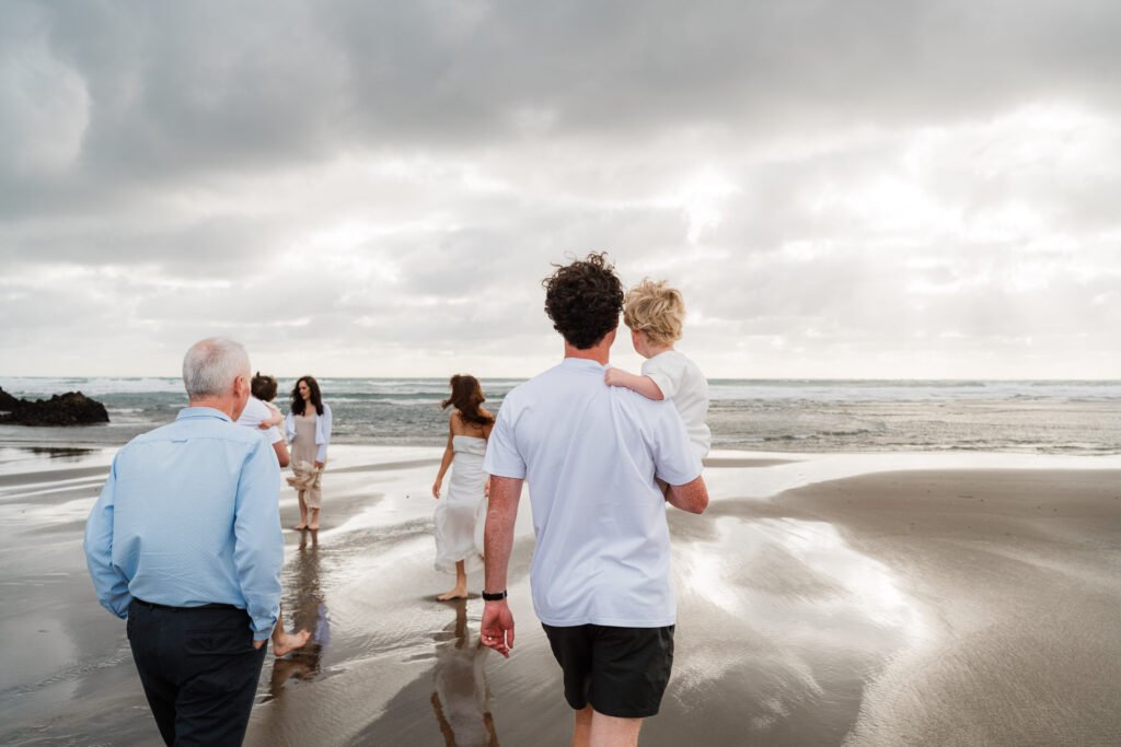 Family walking on beach under cloudy sky, ocean waves visible